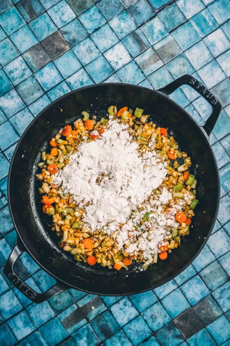 Flour sprinkled in a mound over the softened onion, carrot and celery, the roux step that thickens the soup.