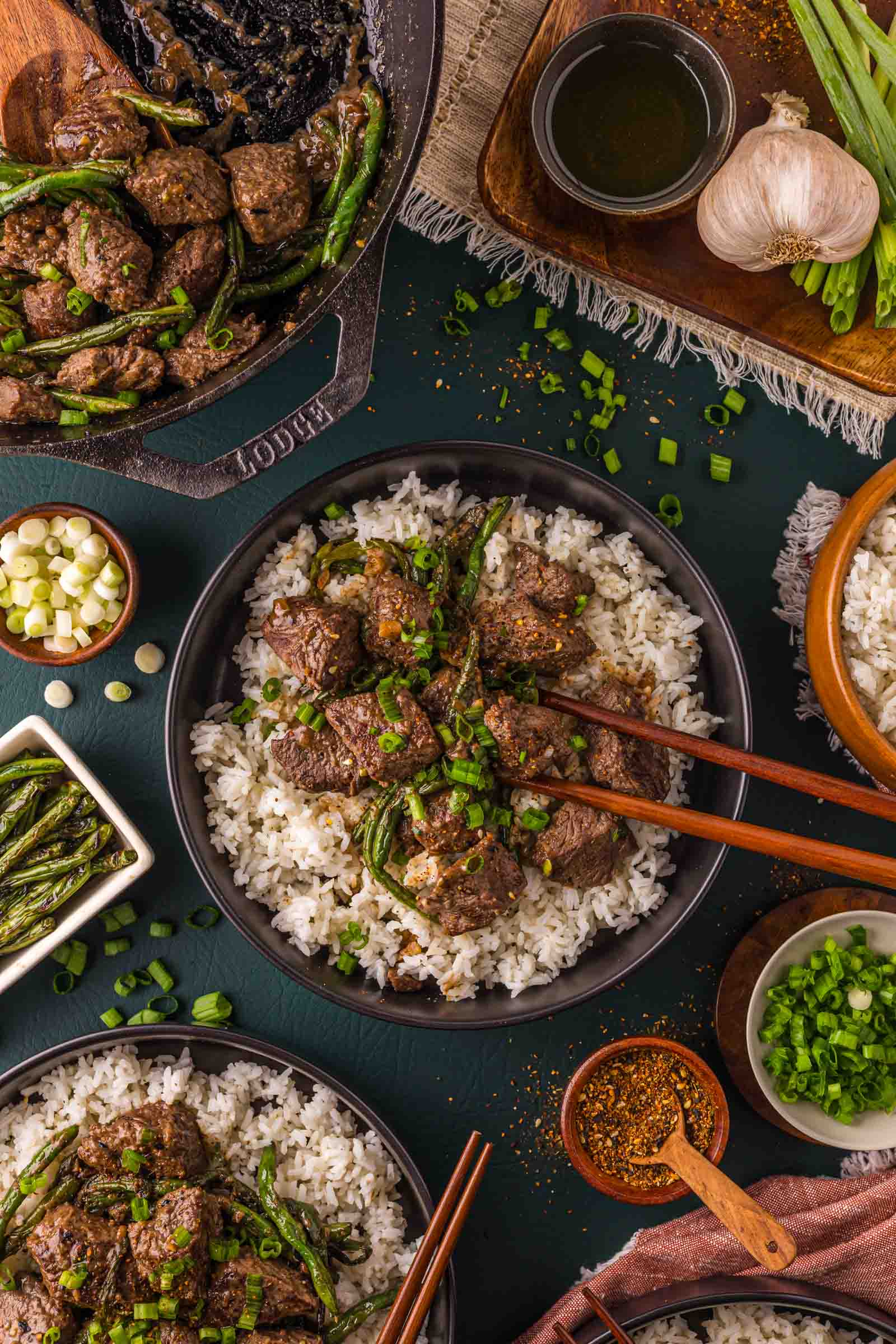 Miso butter steak bites and blistered green beans piled over white rice in a black bowl, with togarashi and scallions alongside.