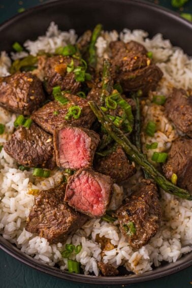 Miso butter steak bites over white rice, two cut open to show pink centers, with blistered green beans and scallion greens.