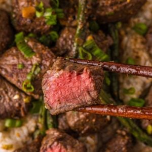 Macro of a miso butter steak bite held in chopsticks, cut to show the pink center, over the bowl of rice and green beans.