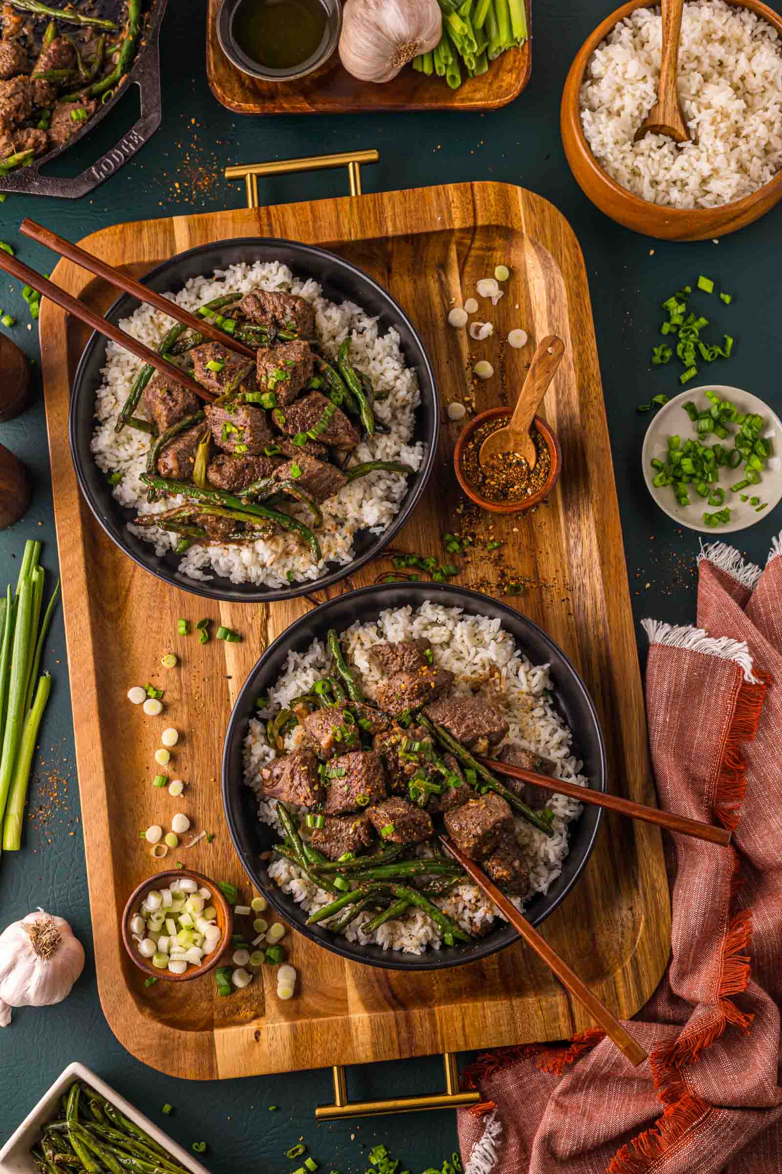 Two bowls of miso butter steak bites over white rice on a wooden tray, with togarashi, scallions and extra rice alongside.