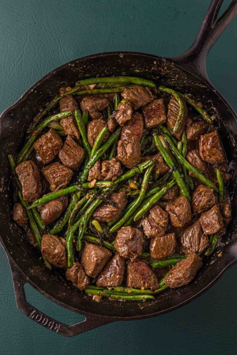 Miso butter steak bites and blistered green beans tossed together in the cast iron skillet, glossy with pan sauce.