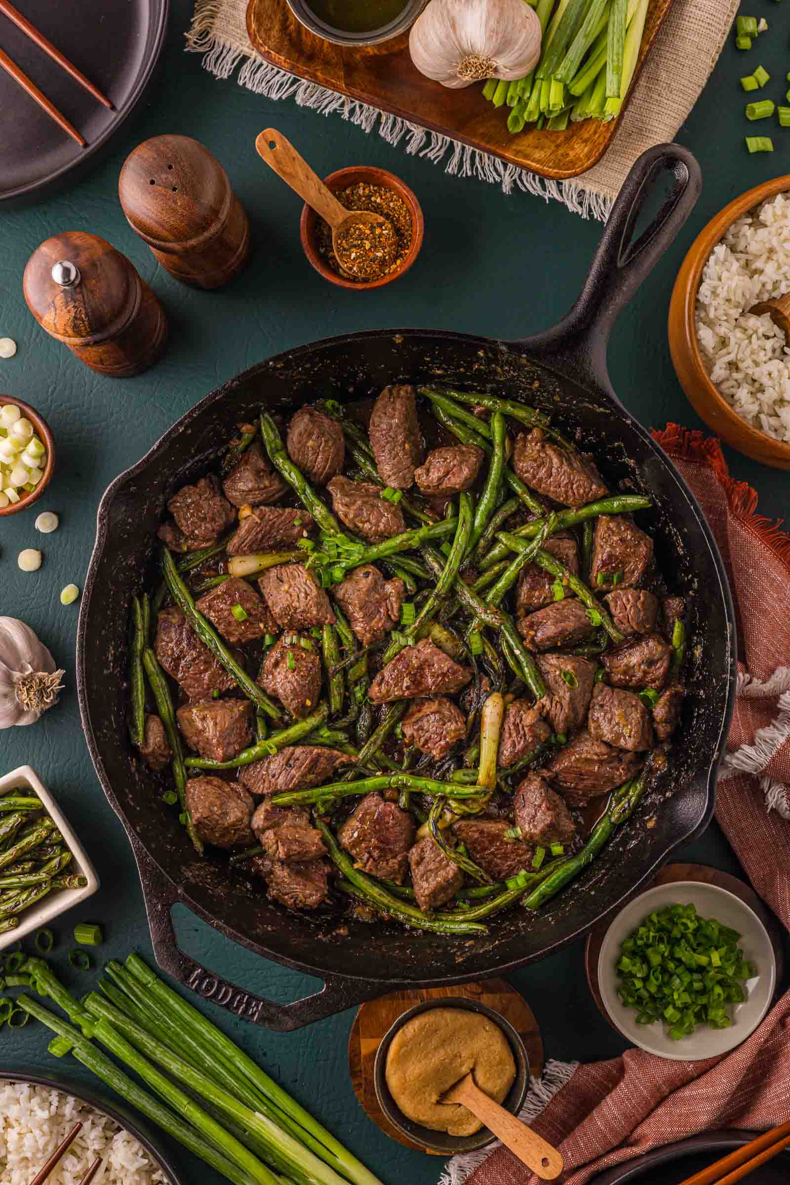Overhead of the finished miso butter steak bites skillet surrounded by white rice, white miso paste, togarashi, sliced scallions and garlic.
