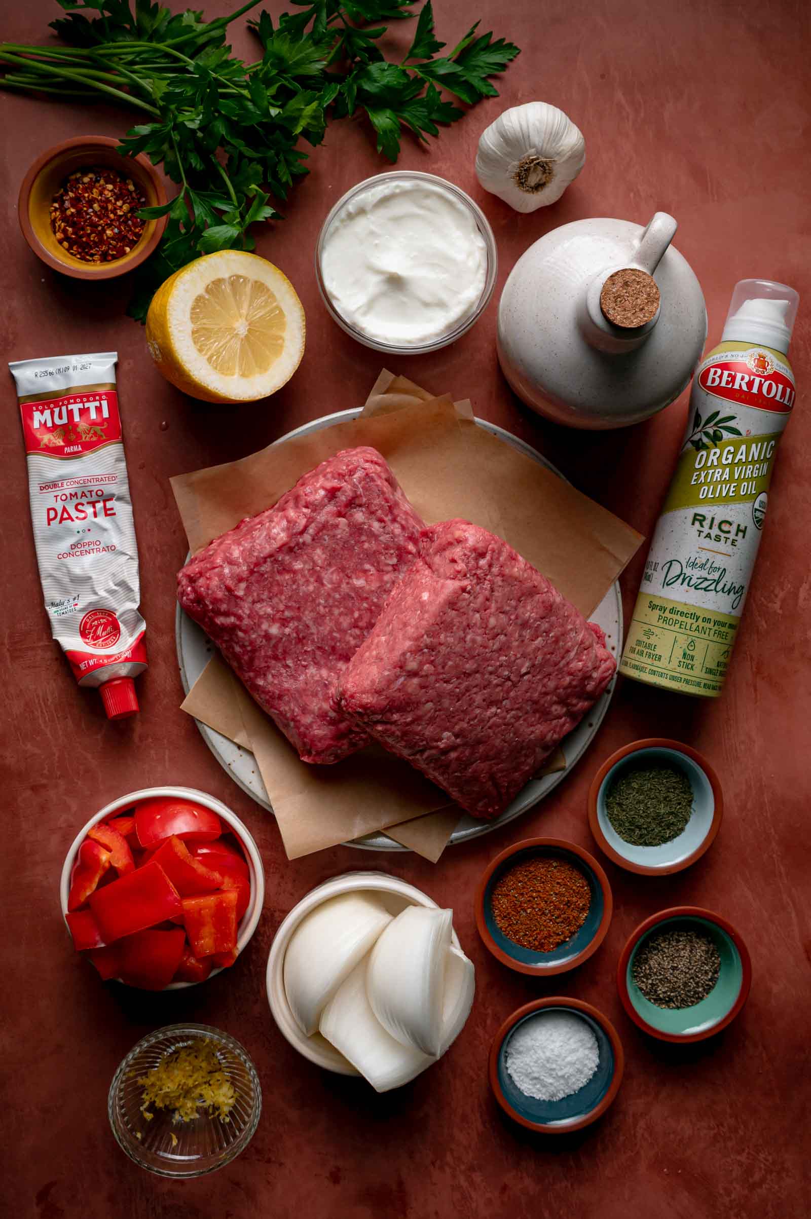 Ingredients for sheet pan kebabs: ground lamb and beef, red bell pepper, onion, garlic, parsley, yogurt, tomato paste, lemon, olive oil and baharat spices.