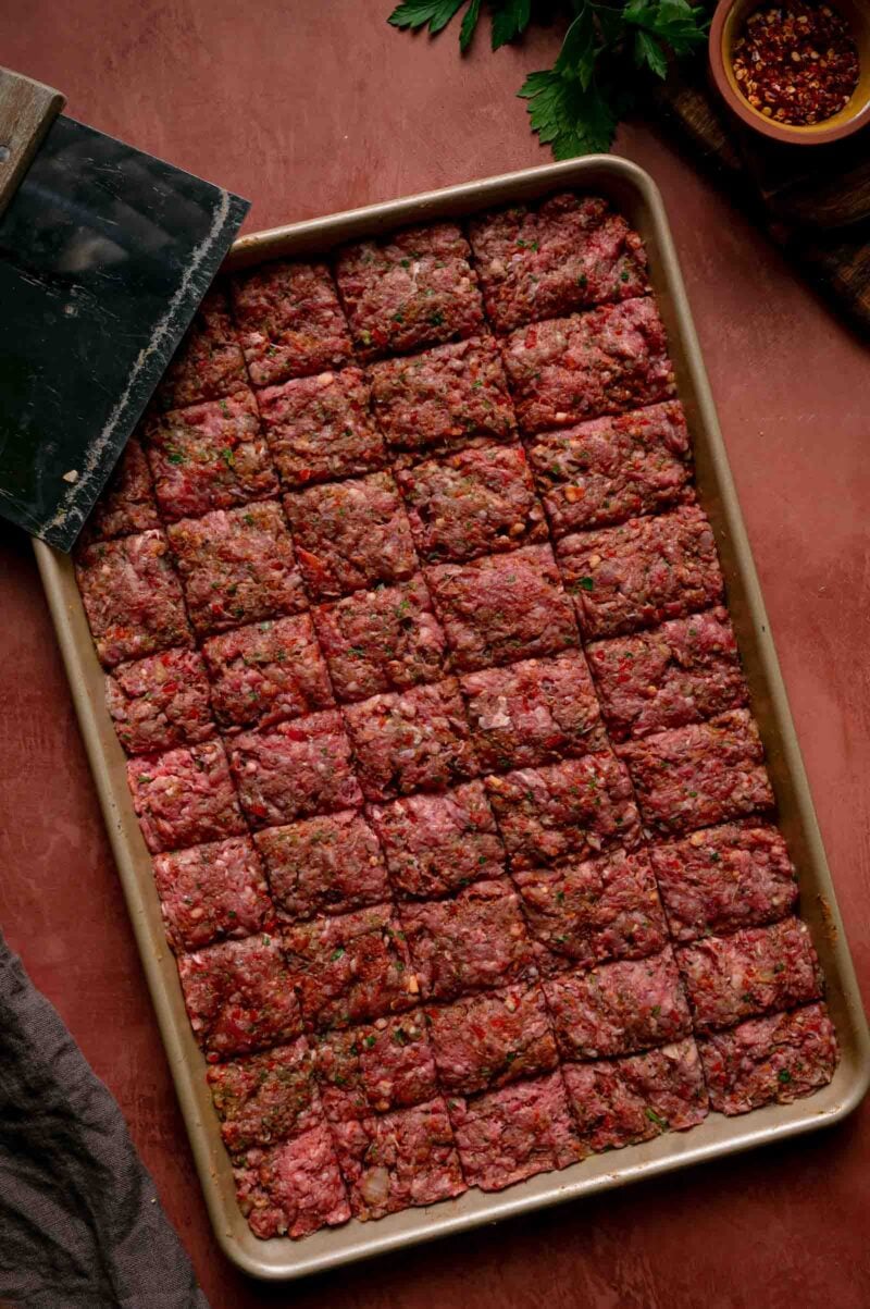 The raw kebab slab scored into even squares on the sheet pan, ready to bake.