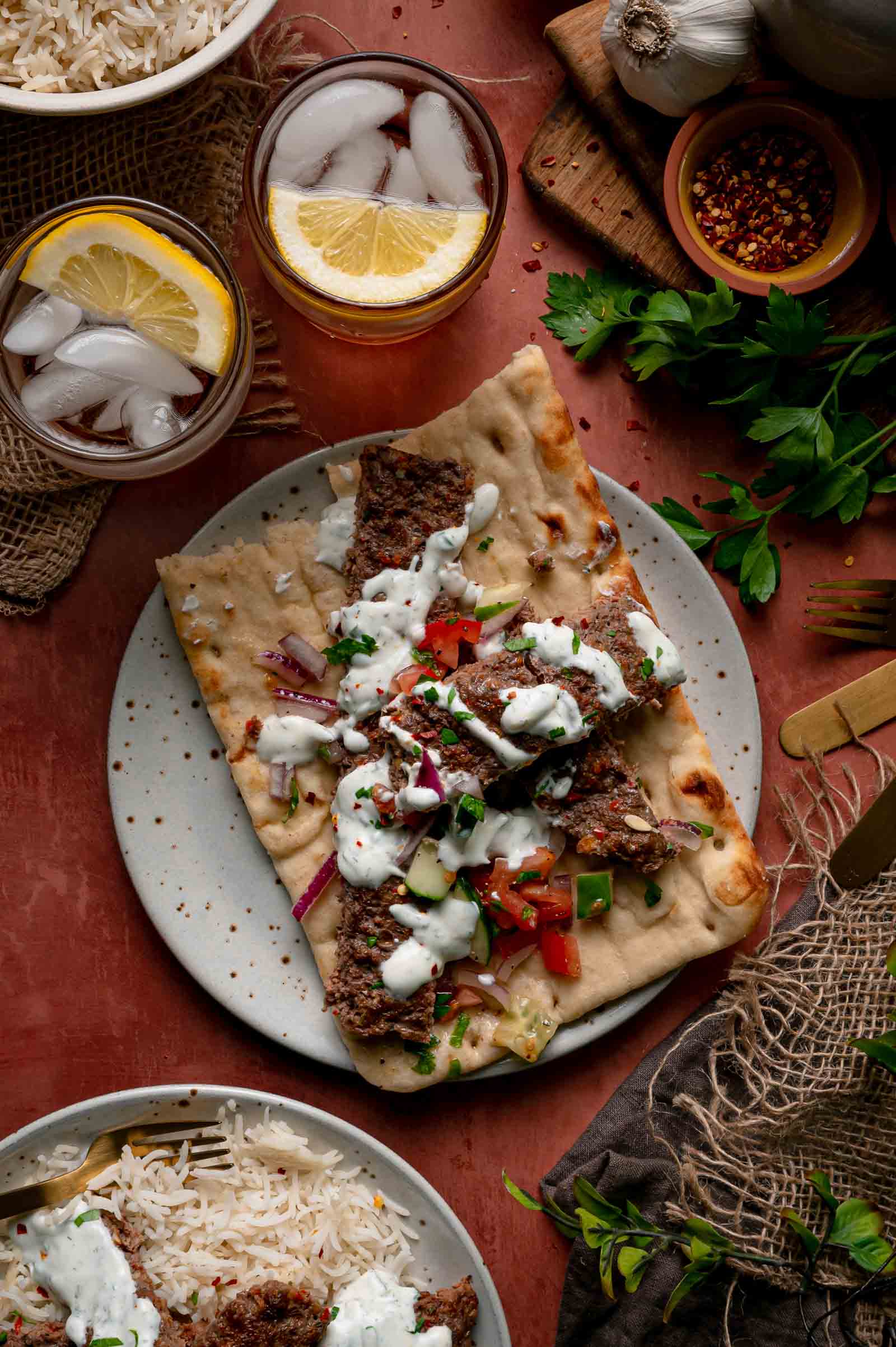 Sheet pan kebabs on flatbread with herbed yogurt sauce and chopped salad, iced tea and rice alongside.