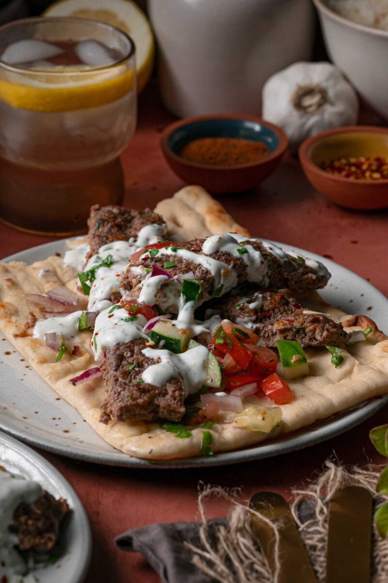 Sheet pan kebabs served on flatbread with herbed yogurt sauce, chopped tomato, cucumber and red onion.