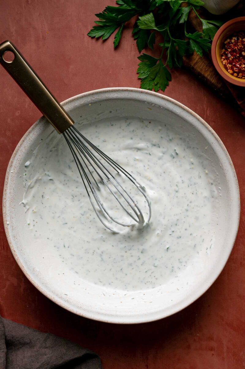 The herbed yogurt sauce whisked smooth, whisk resting in the bowl.