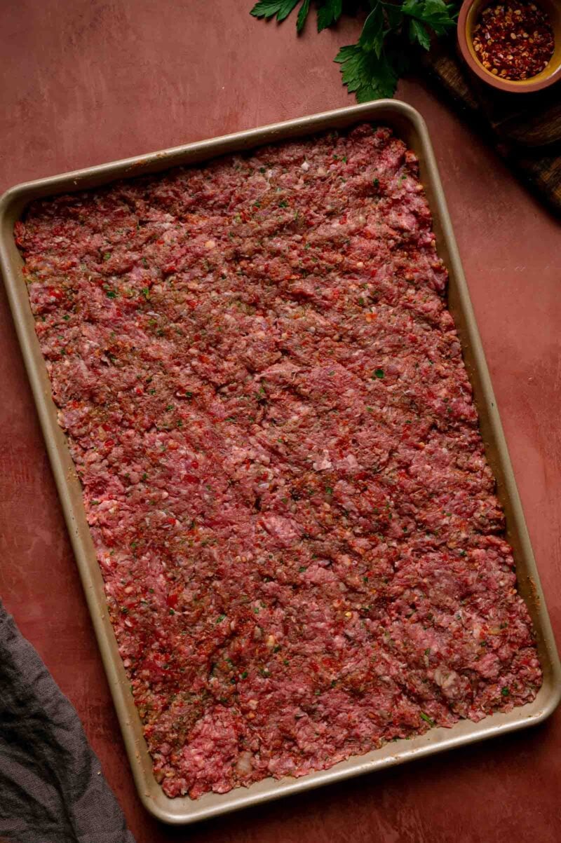 The seasoned lamb and beef kebab mixture pressed in an even layer across a sheet pan.