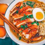 Overhead bowl of teriyaki chicken ramen, sliced chicken glazed in teriyaki beside a halved jammy egg and curled ramen noodles.