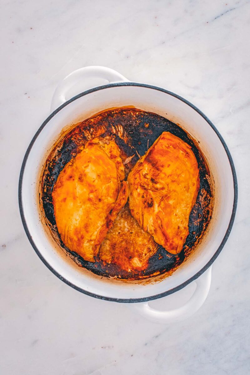 The marinated chicken breasts seared deep golden on both sides in a Dutch oven, not yet cooked through.