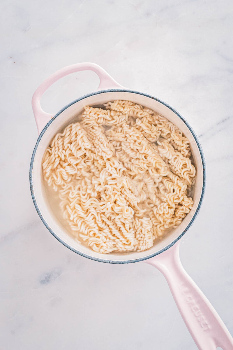 Ramen noodles cooking in their own saucepan of water, kept separate so the broth stays clear.