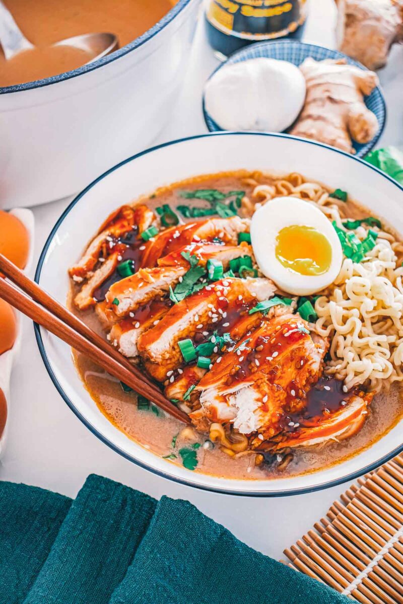 A bowl of teriyaki chicken ramen with sliced chicken, a jammy soft-boiled egg, noodles, green onion and sesame seeds.