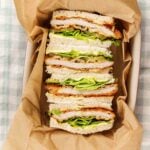 Tonkatsu sandwiches stood on end in a parchment lined dish, breaded pork cutlet, chopped greens and pickle slices between crustless white bread.