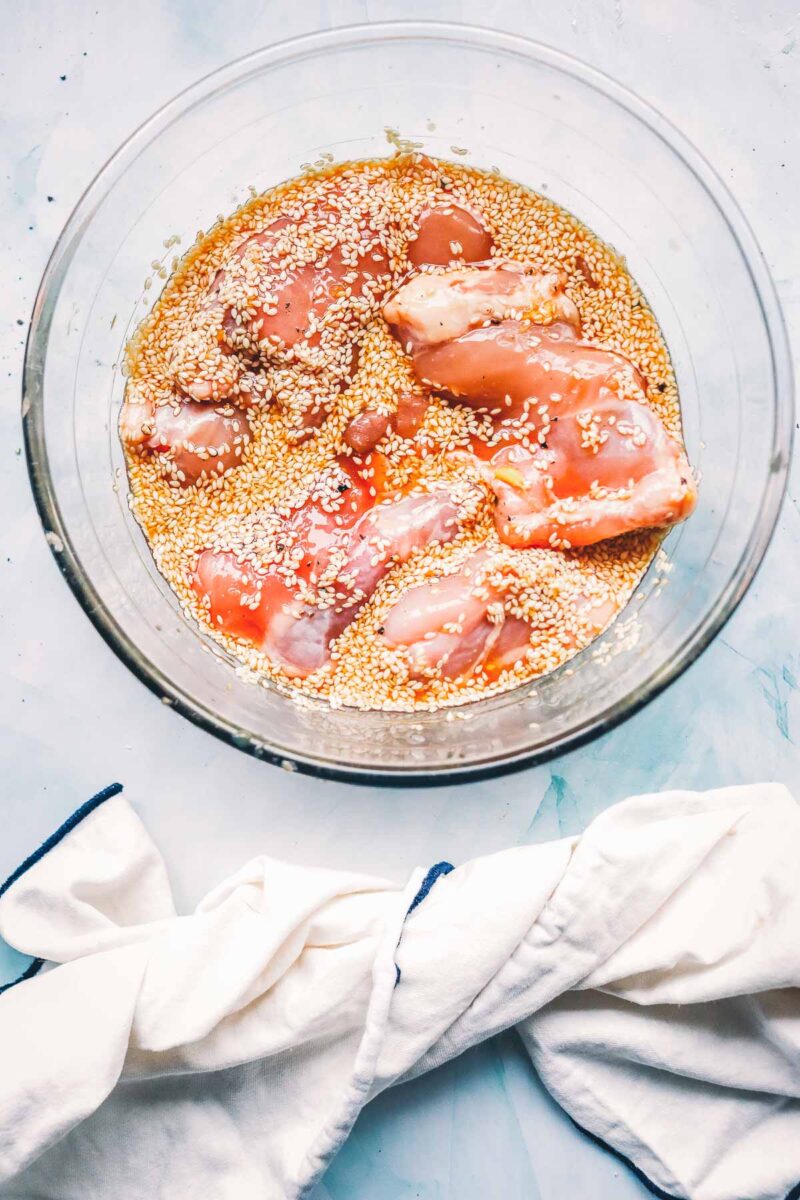 Raw chicken thighs soaking in the soy, honey and sesame teriyaki marinade in a glass bowl, ready to go into the fridge.