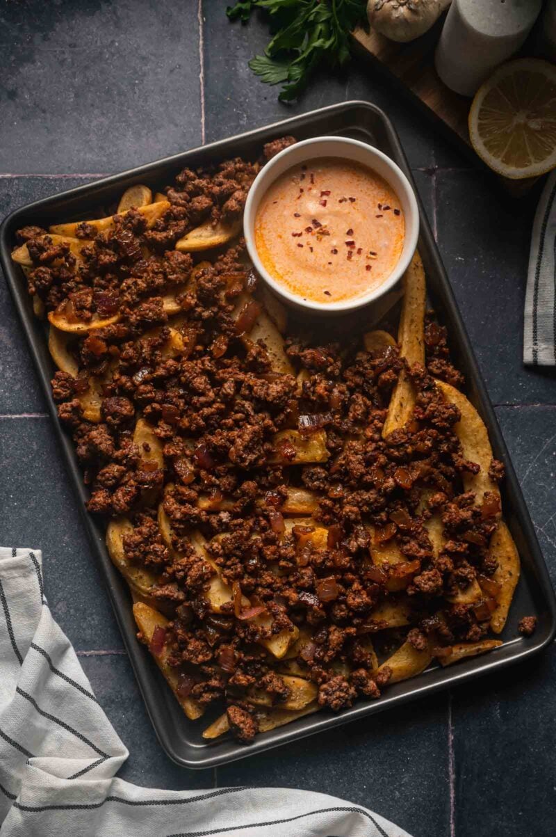 The spiced ground lamb spooned over the baked fries on the sheet pan, with a ramekin of harissa yogurt sauce.