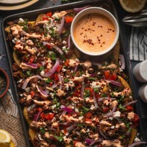 A sheet pan of Greek feta fries with the harissa yogurt sauce drizzled over the lamb, feta, tomato and red onion.