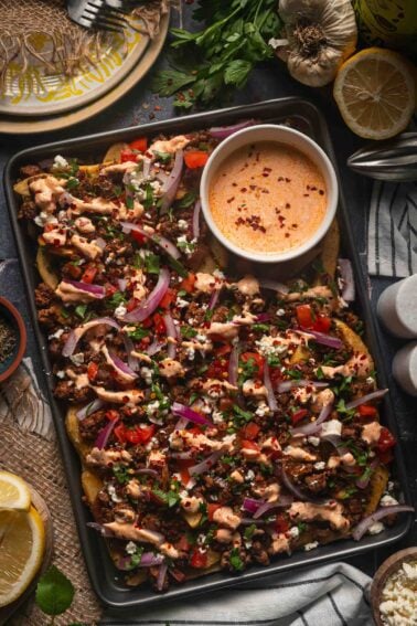 A sheet pan of Greek feta fries with the harissa yogurt sauce drizzled over the lamb, feta, tomato and red onion.
