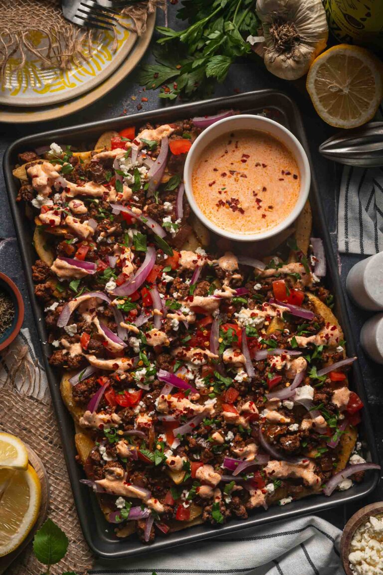 A sheet pan of Greek feta fries with the harissa yogurt sauce drizzled over the lamb, feta, tomato and red onion.