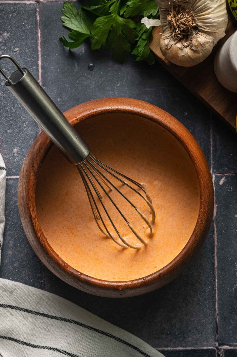 The harissa yogurt sauce whisked smooth in a wooden bowl, thinned until it pours in a ribbon.