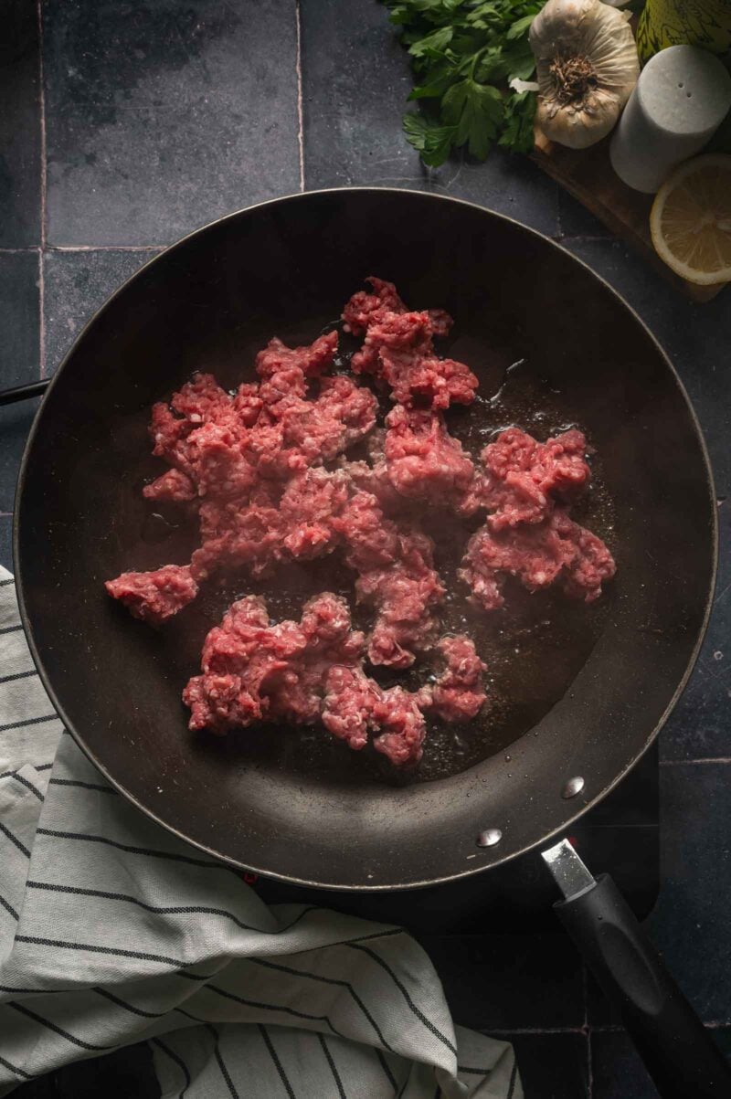 Raw ground lamb pressed flat in a hot skillet, left undisturbed to brown on the bottom.