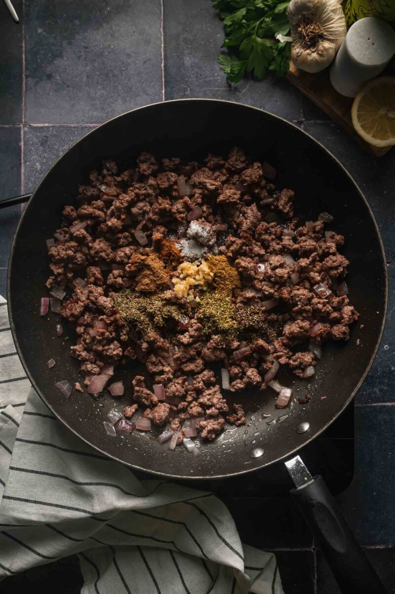 Cumin, coriander, oregano, thyme, rosemary, cinnamon and minced garlic mounded over the ground lamb and onion in the skillet.