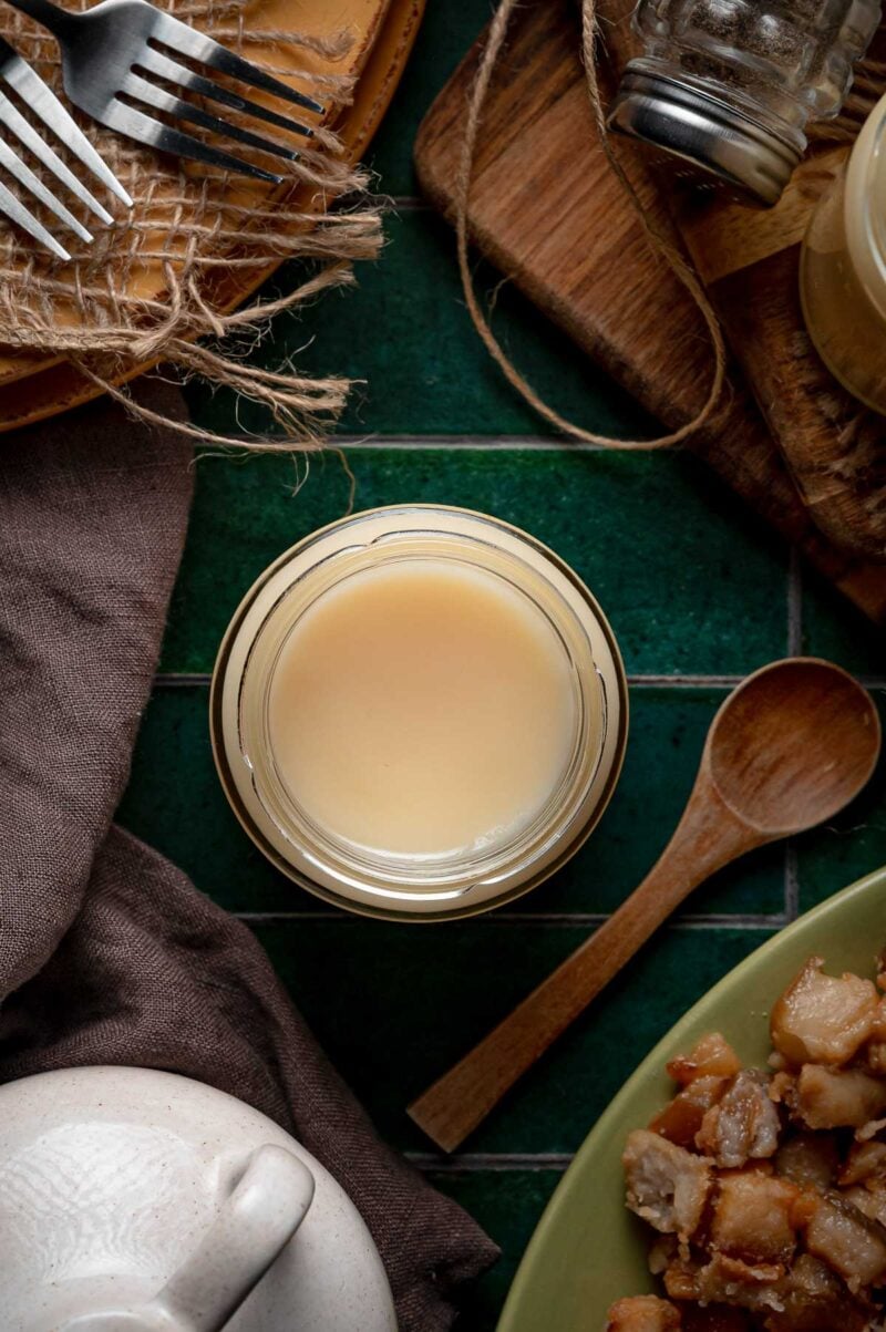 A jar of slow cooker lard chilled firm and pale cream, with a plate of crisp pork cracklings and a wooden spoon alongside.