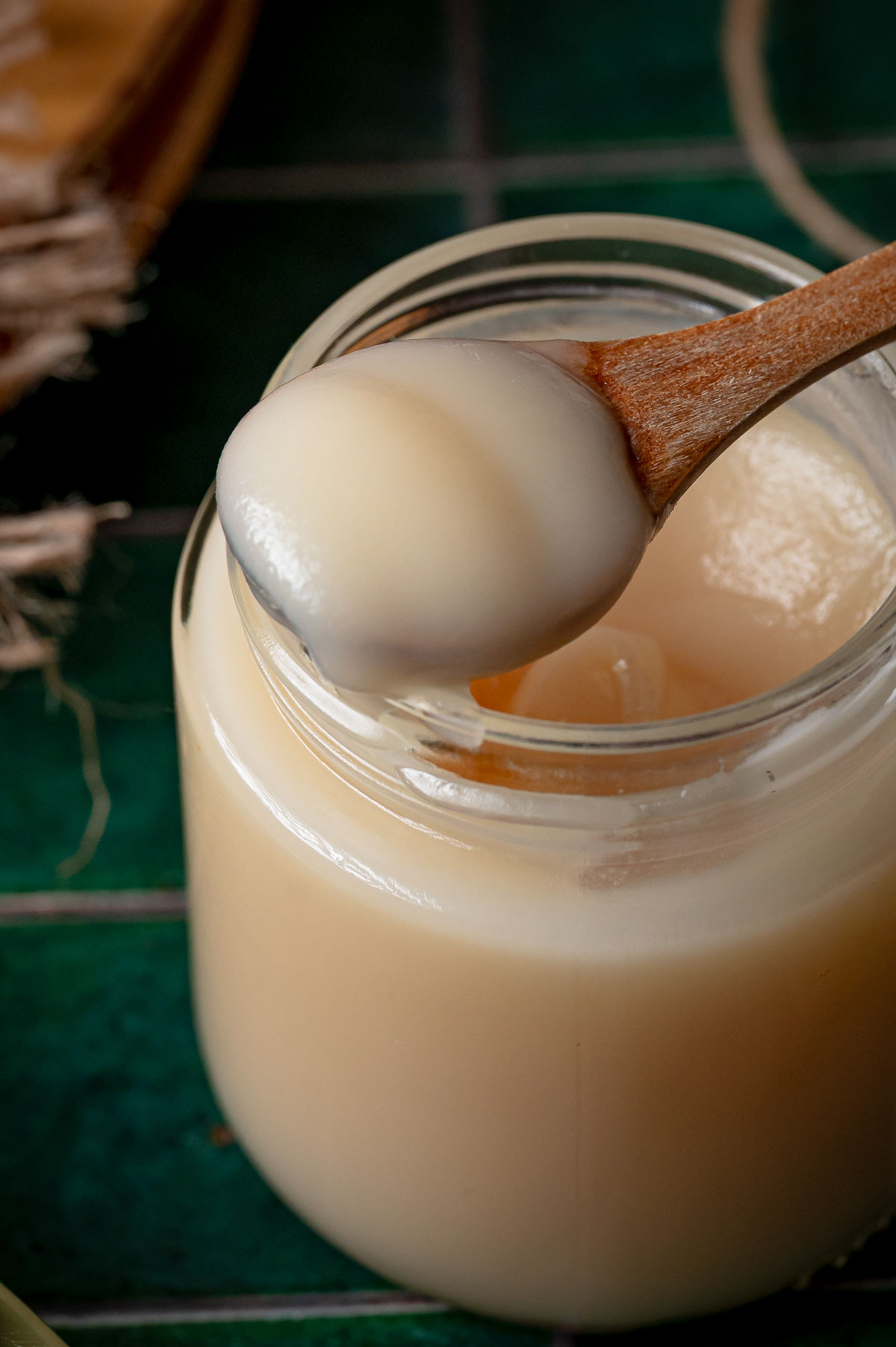 A wooden spoon lifting a scoop of set rendered lard from the jar, showing the smooth spreadable texture of a finished render.