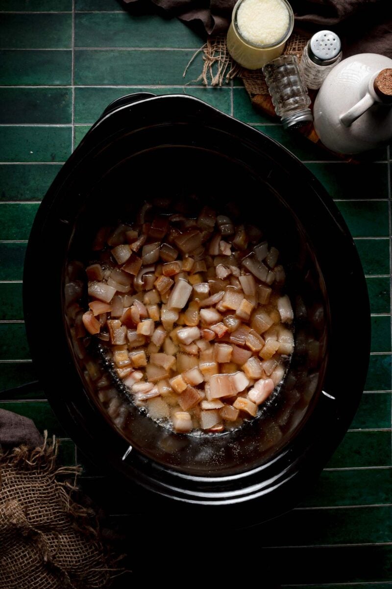 Pork fat about two hours into rendering, with a shallow pool of clear melted lard collecting around cubes that are still pale.