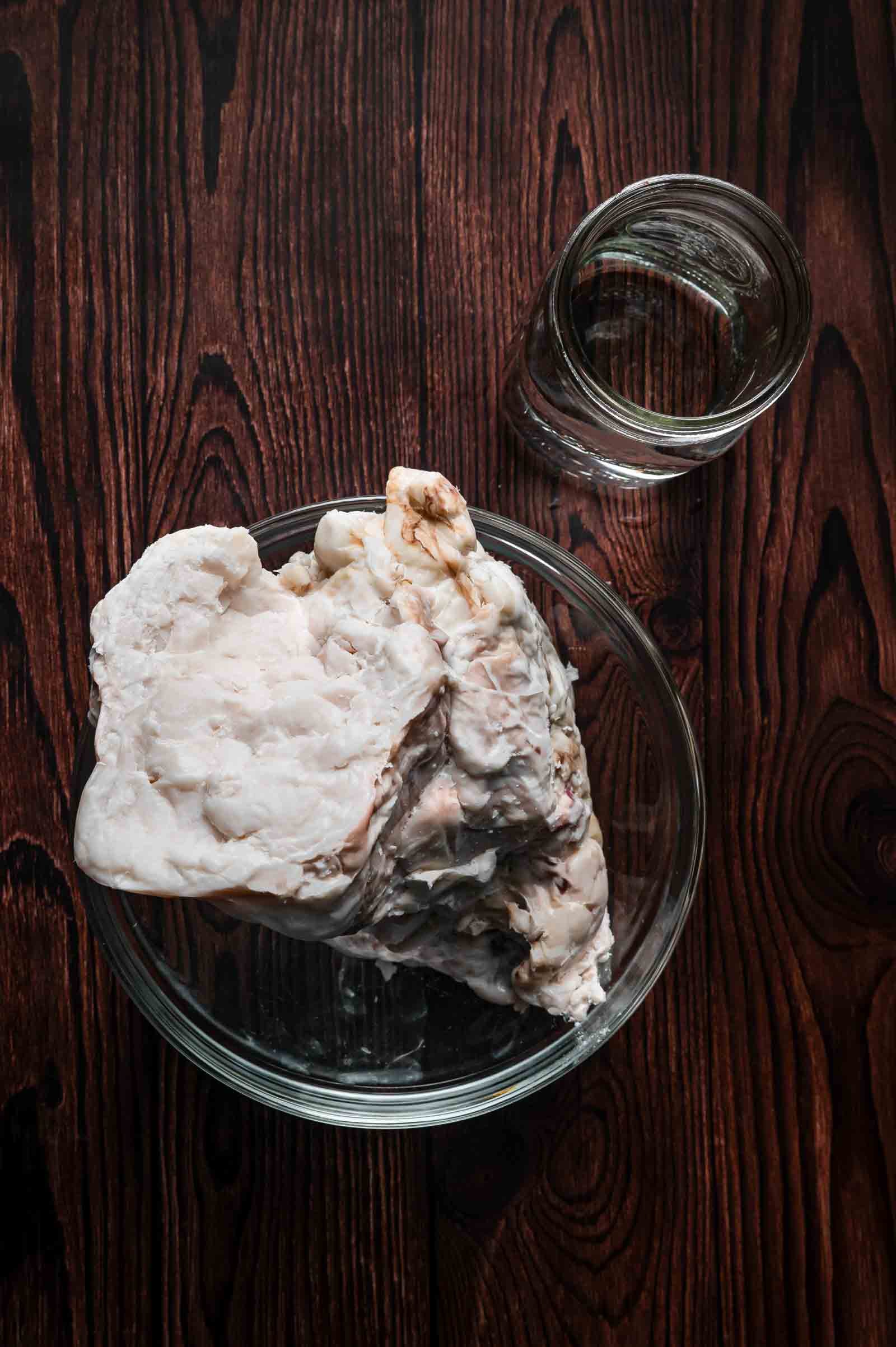 A whole slab of hard white beef fat trimmed off a brisket, resting in a glass bowl beside a glass of water before rendering.