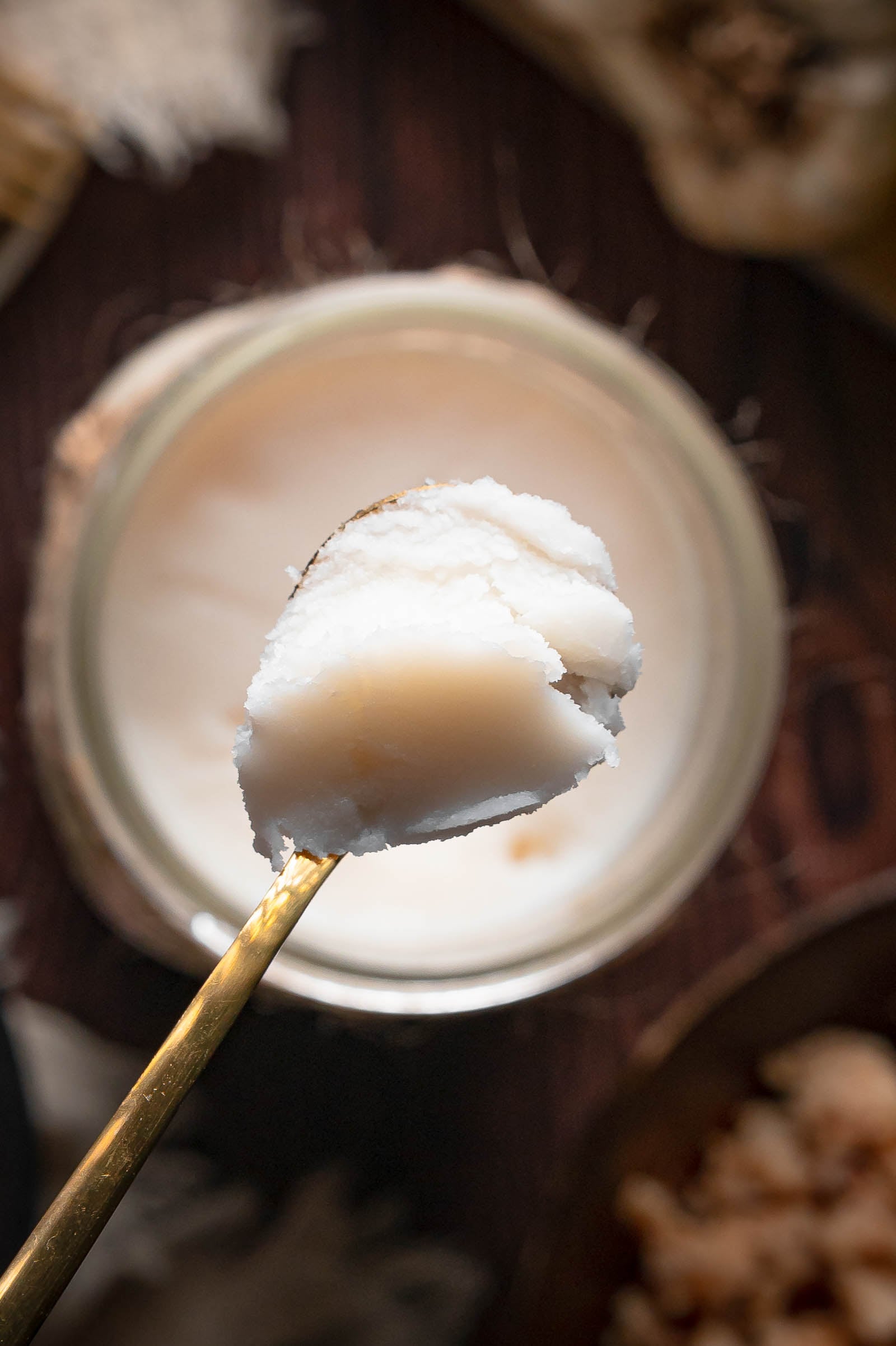 A spoon lifting a scoop of set beef tallow from the jar, showing the firm, smooth texture it holds when chilled.