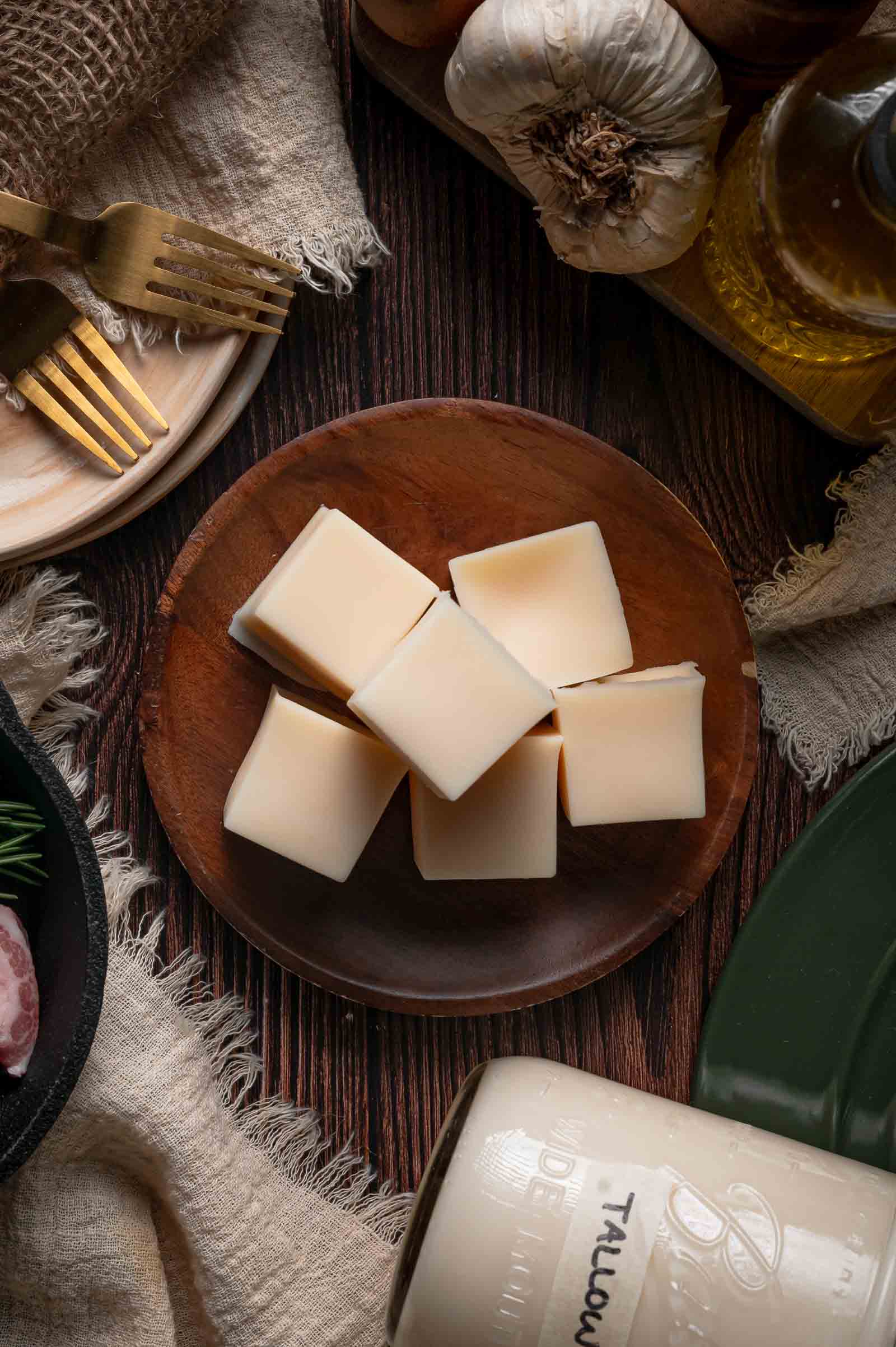 Six cubes of solid beef tallow on a wooden plate, molded and cooled for easy portioning, with the labeled jar alongside.