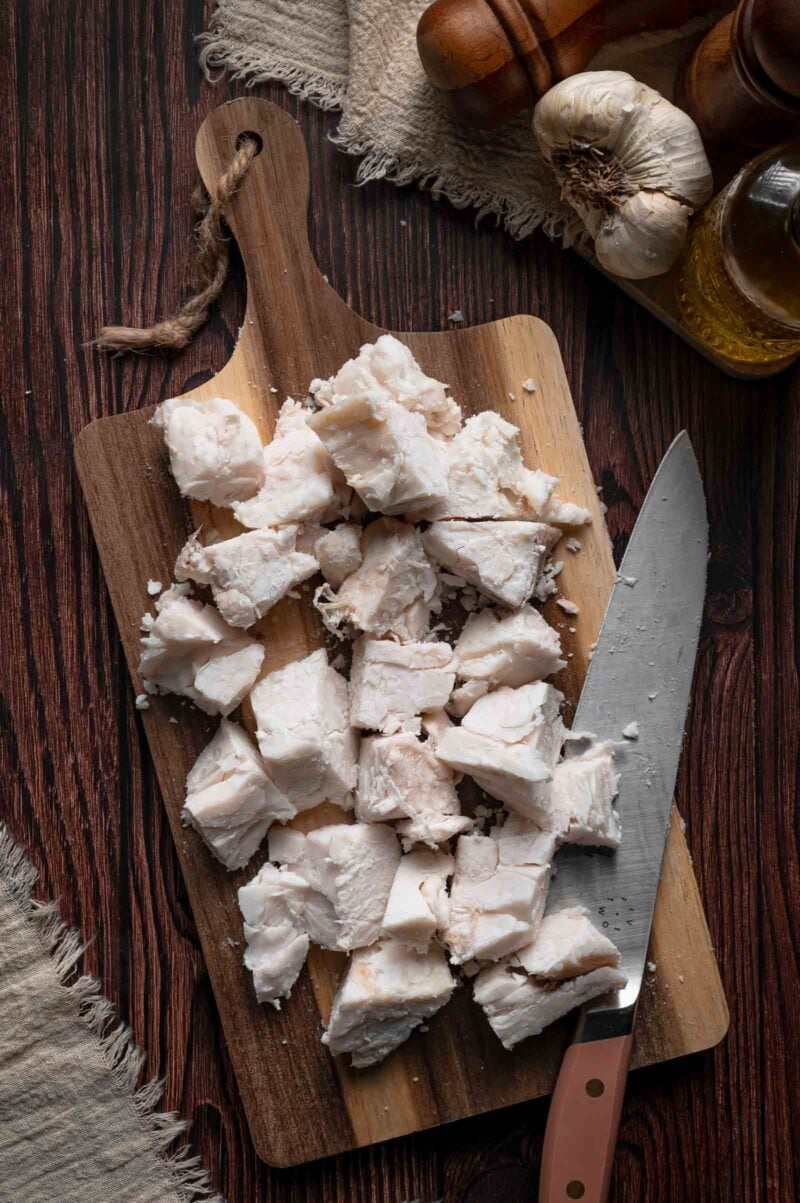 Hard beef fat trimmings chopped into half inch pieces on a wooden cutting board with a chef's knife, ready to render.