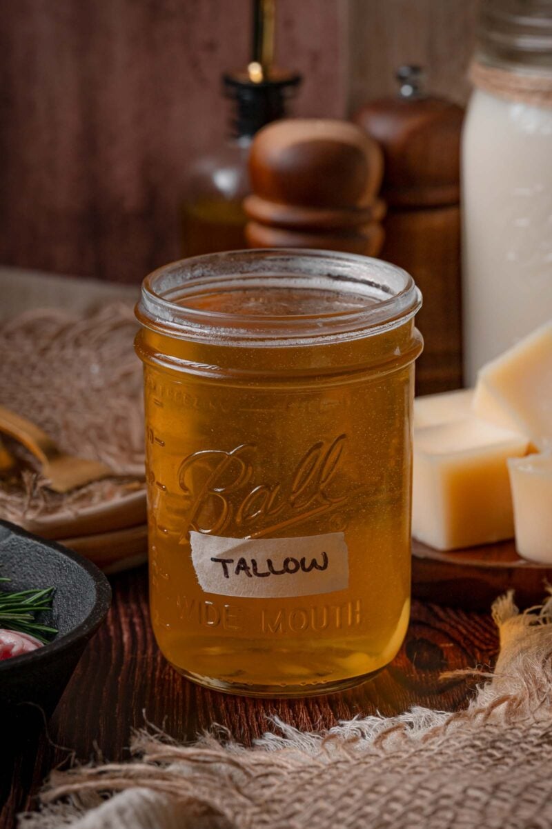 A mason jar labeled tallow filled with warm liquid beef tallow, still golden and clear before it cools and sets opaque.