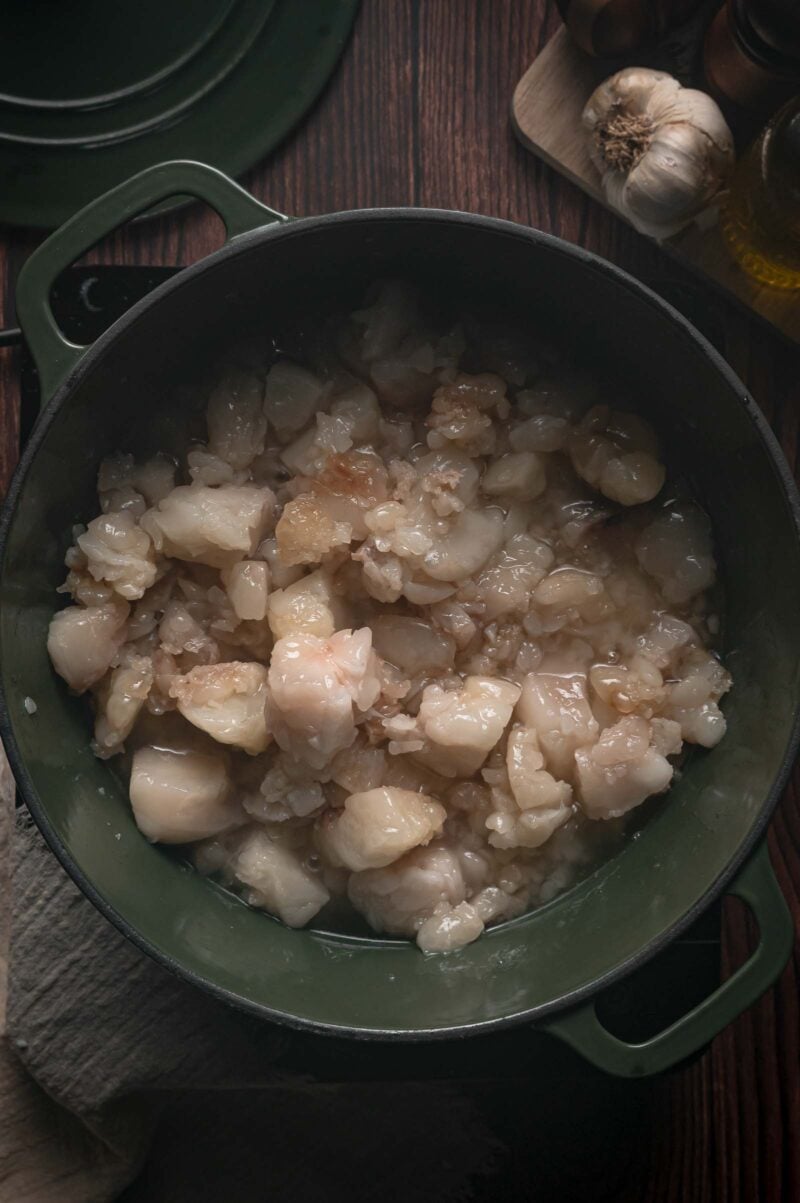 Beef fat partway through rendering, the pieces gone soft and translucent with clear liquid tallow pooling around them.