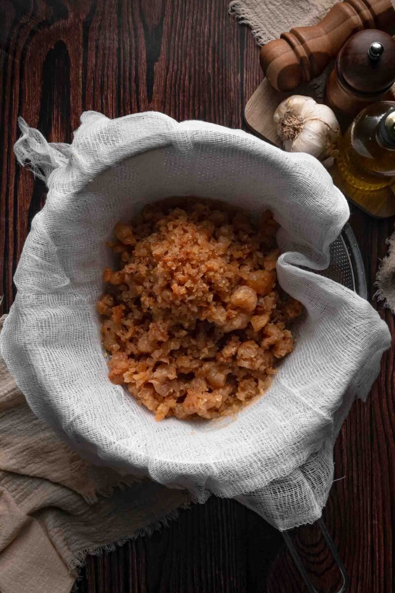 Rendered beef cracklings caught in a double layer of cheesecloth inside a fine mesh strainer after the tallow drained through.