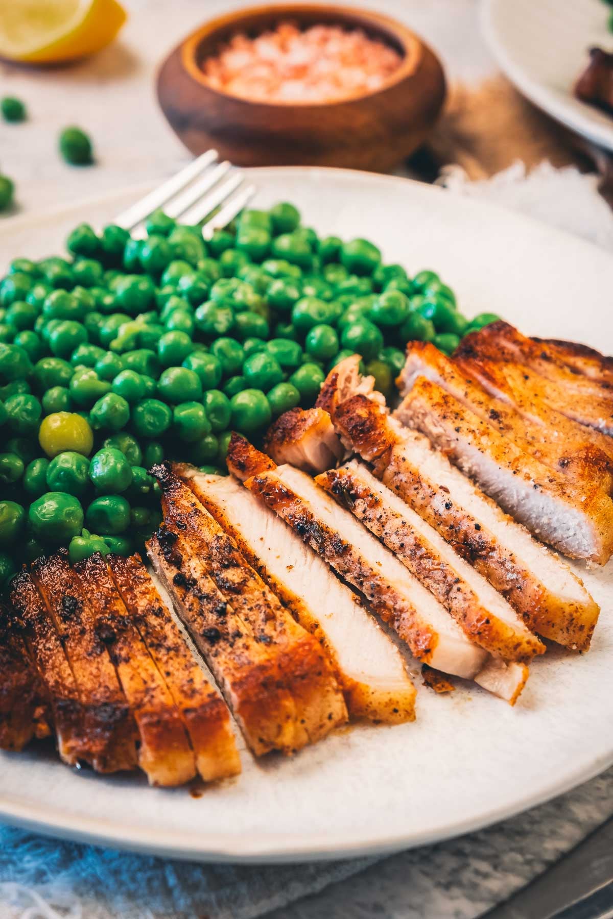 Close-up of a pork chop sliced into strips next to green peas, each slice edged with a golden seared crust.