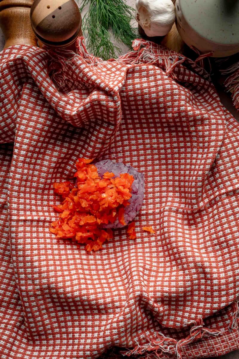 Grated red bell pepper and red onion piled on a kitchen towel, ready to be wrung out so the tortilla kebab layers stay dry.
