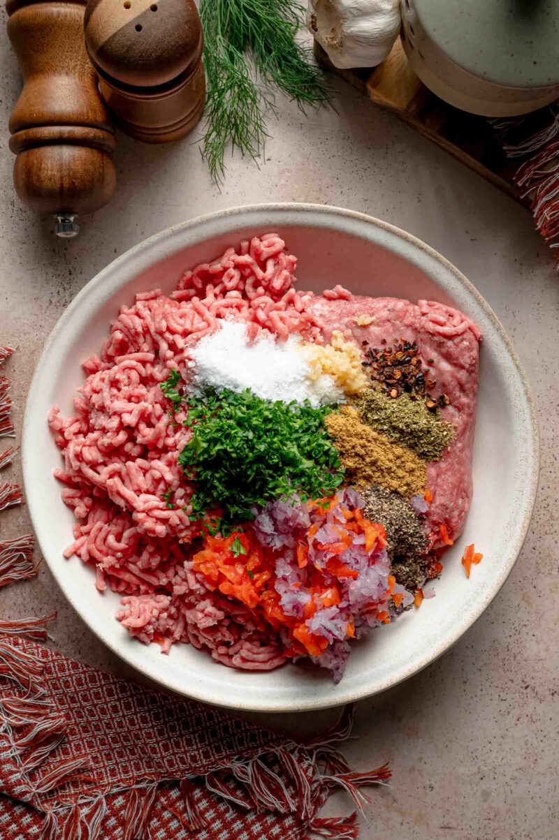 Ground lamb and ground beef in a bowl with kosher salt, minced garlic, Aleppo pepper, cumin, oregano, black pepper, parsley and the grated vegetables.