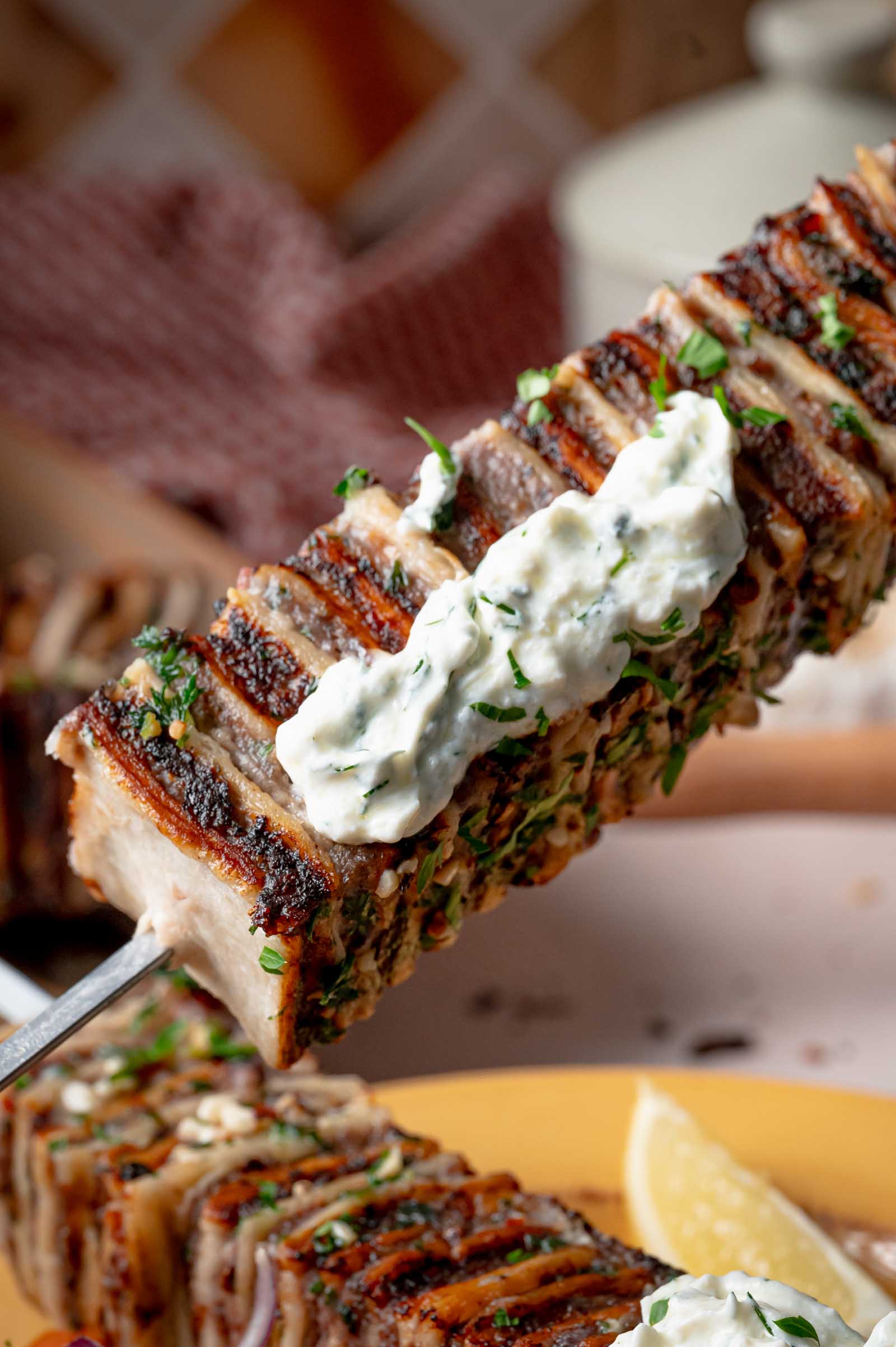Close up of a tortilla kebab skewer topped with cold haydari and chopped parsley, every tortilla layer crisp at the edge.