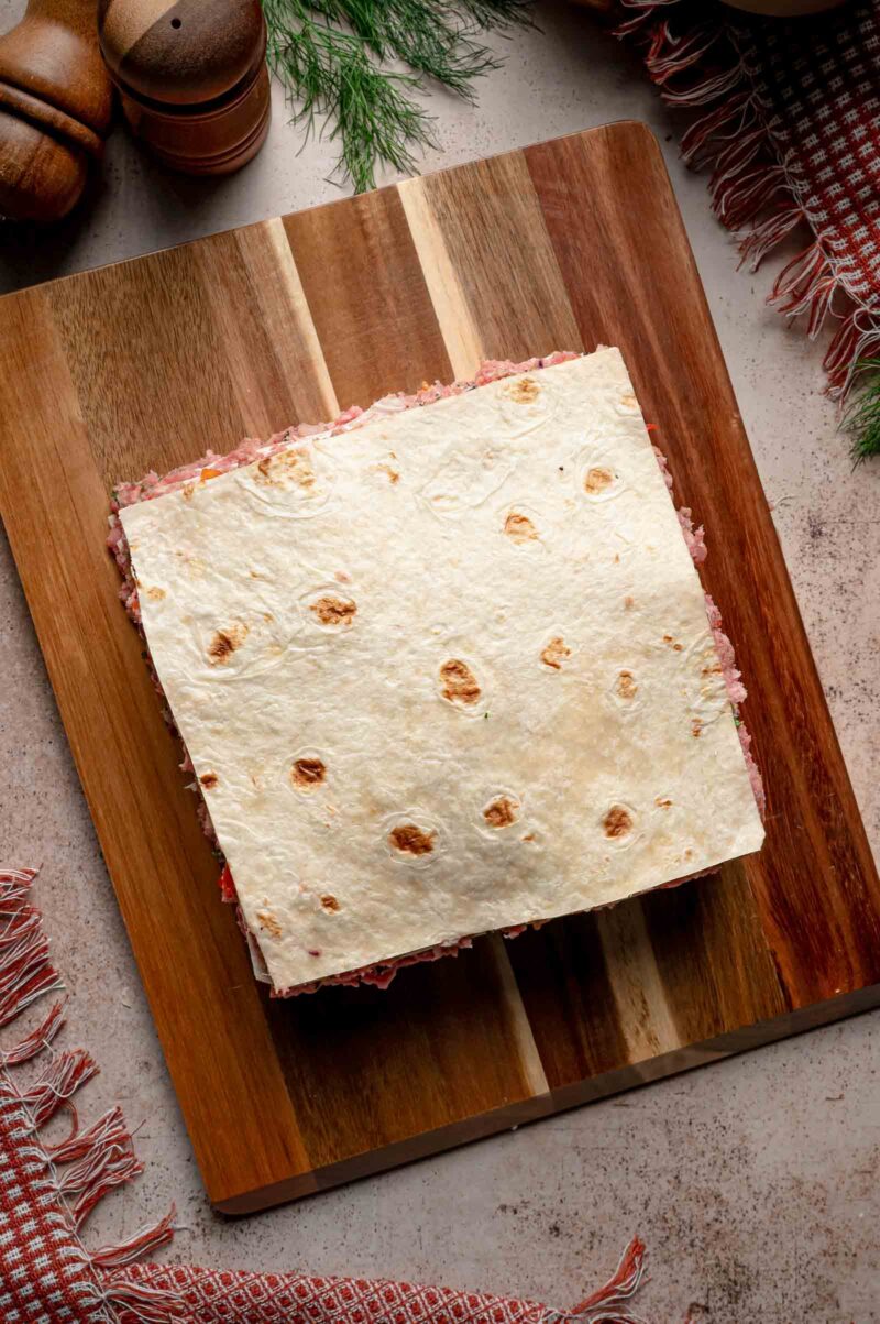 Another squared tortilla laid over the meat layer, building the stack that becomes the tortilla kebab skewers.