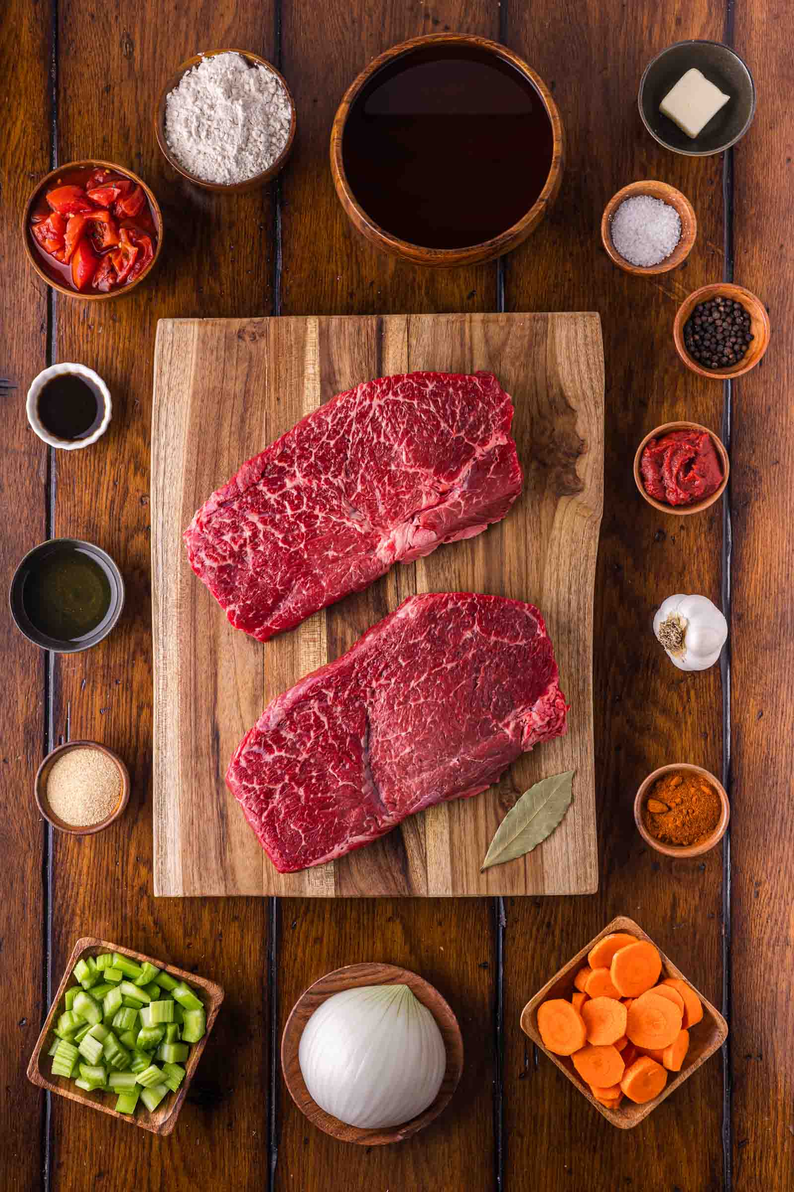 Ingredients for Swiss steak: raw beef round steaks, flour, broth, crushed tomatoes, tomato paste, carrots, celery, onion, garlic, paprika and a bay leaf.