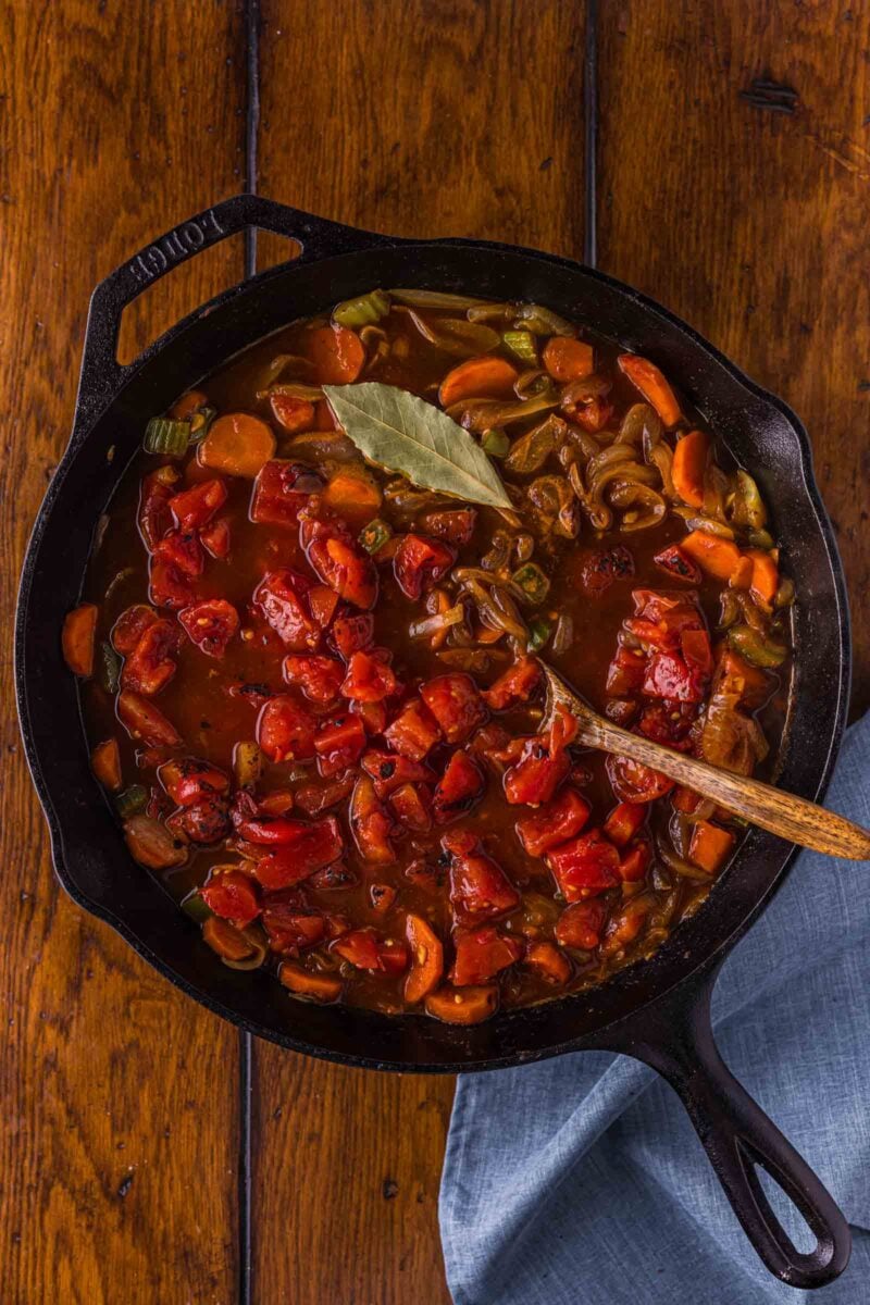 Crushed tomatoes and a bay leaf stirred into the vegetables in the cast iron skillet, building the braising gravy.