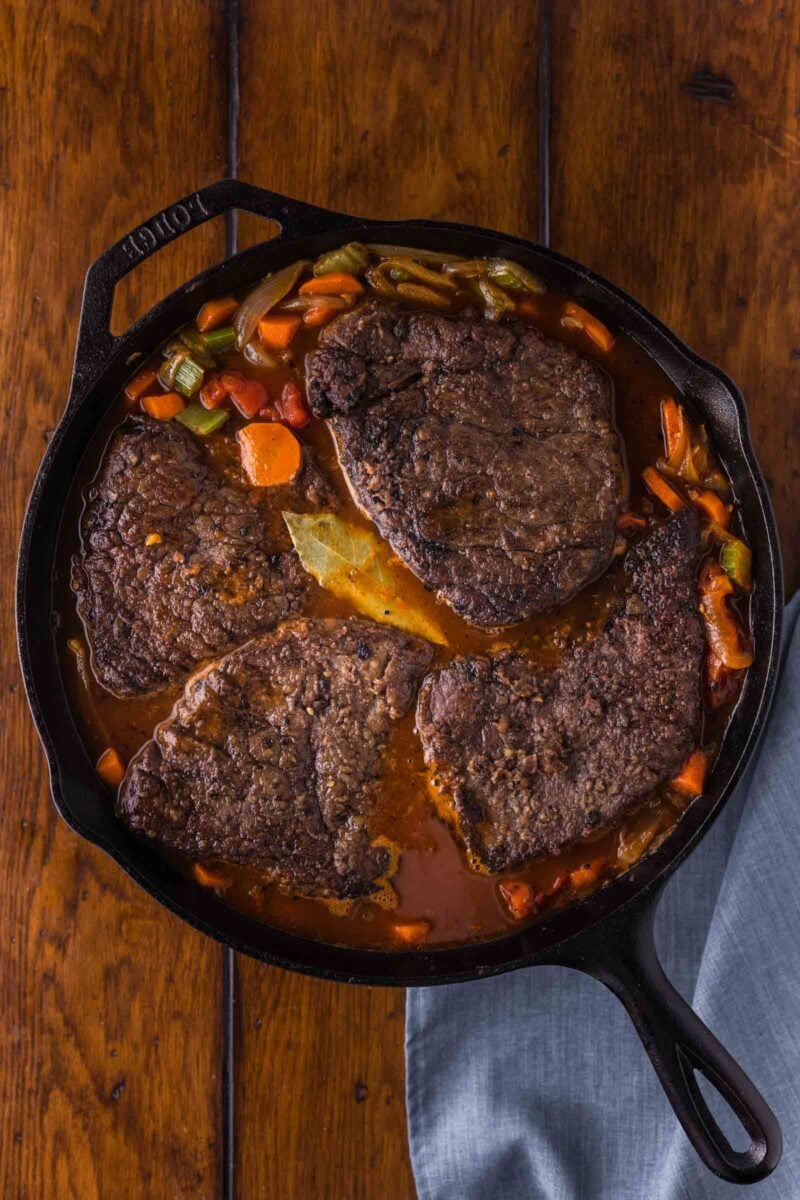 Four seared round steaks nestled back into the tomato gravy with carrots, celery and a bay leaf, ready for the oven.