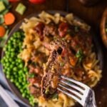 A forkful of Swiss steak lifted above the plate, tomato gravy clinging to the tender beef over the noodles and peas.