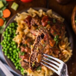 A forkful of Swiss steak lifted above the plate, tomato gravy clinging to the tender beef over the noodles and peas.
