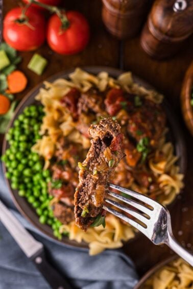 A forkful of Swiss steak lifted above the plate, tomato gravy clinging to the tender beef over the noodles and peas.