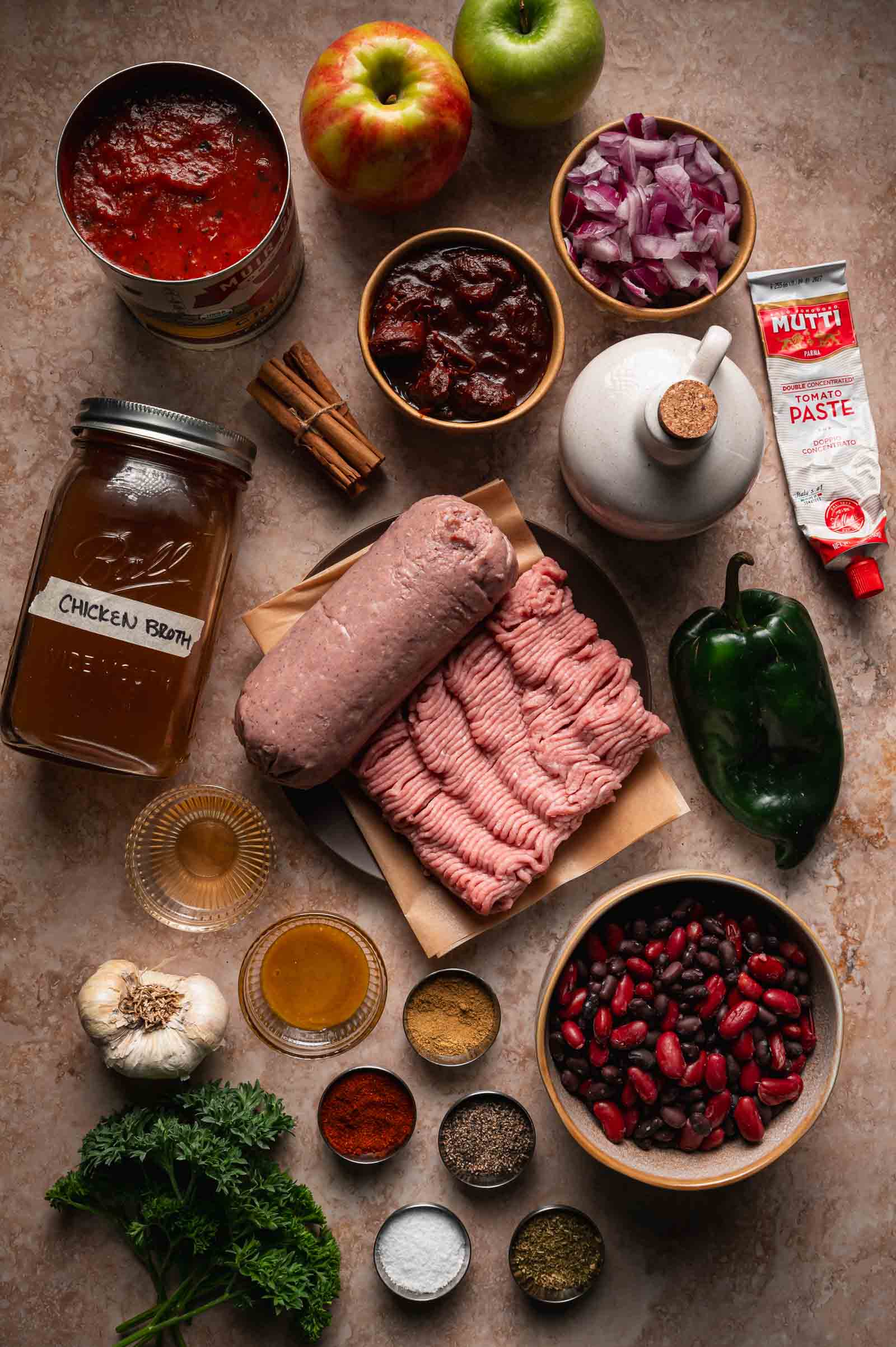 Ingredients for turkey apple chili: ground turkey, red and green apples, a poblano, black and kidney beans, chipotles in adobo, crushed tomatoes, tomato paste, chicken broth, red onion, garlic and cinnamon.