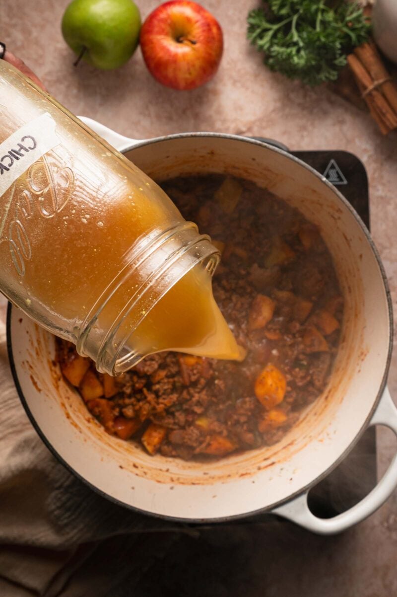 Chicken broth poured from a Ball jar into the pot of ground turkey and apples.