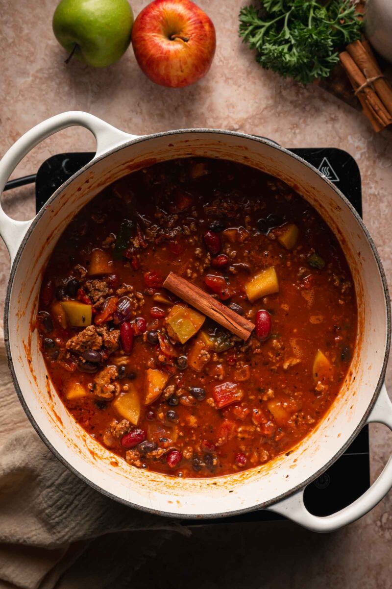 A cinnamon stick resting on top of the turkey apple chili as it simmers with apple chunks and beans.